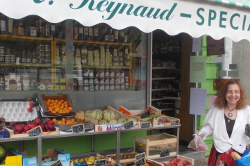 eine Frau steht lachend vor einem kleinen französischem Lebensmittelgeschäft 